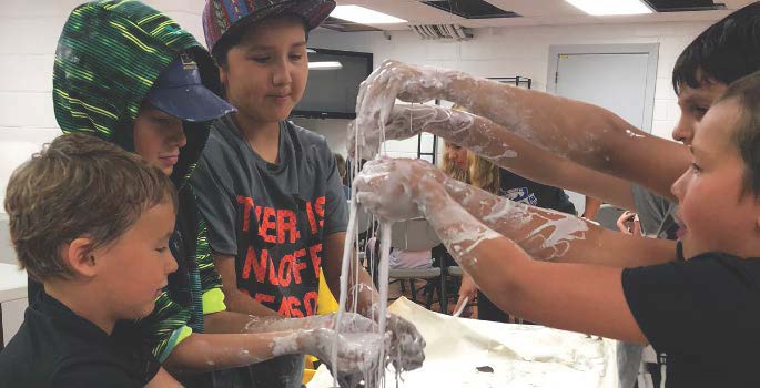 kids with their hands in a pan of slime